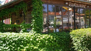 Un restaurant à la façade en bois, doté de grandes fenêtres et agrémenté de verdure.