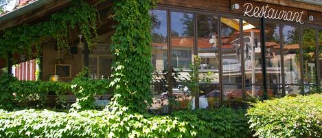 Un restaurant à la façade en bois, doté de grandes fenêtres et agrémenté de verdure.