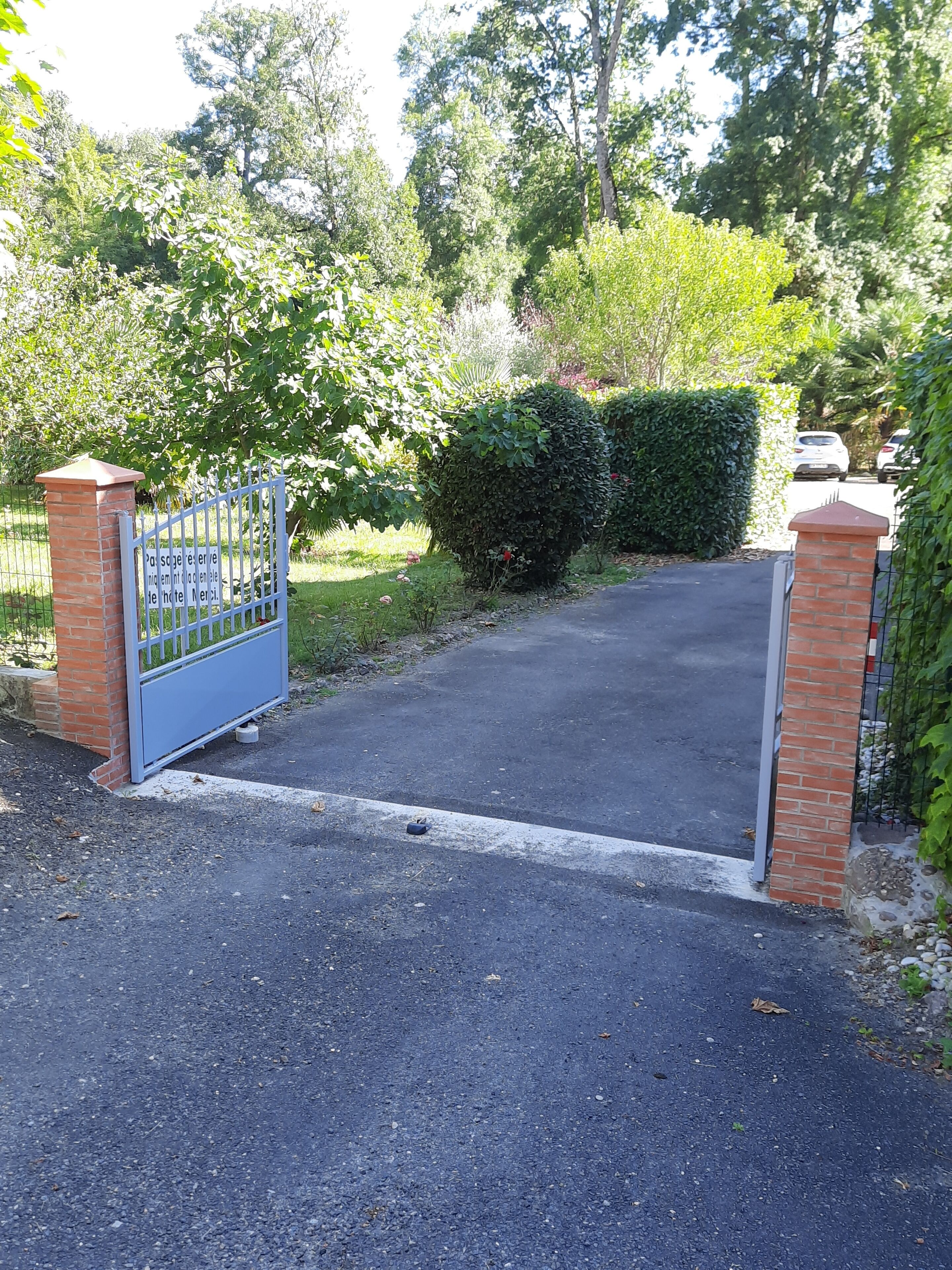 Une allée fermée par un portail mène à un bâtiment agrémenté d’un pilier en briques et d’une porte en métal.