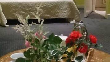 A room with a bed, a small table with a vase of flowers, and a door leading to another room.