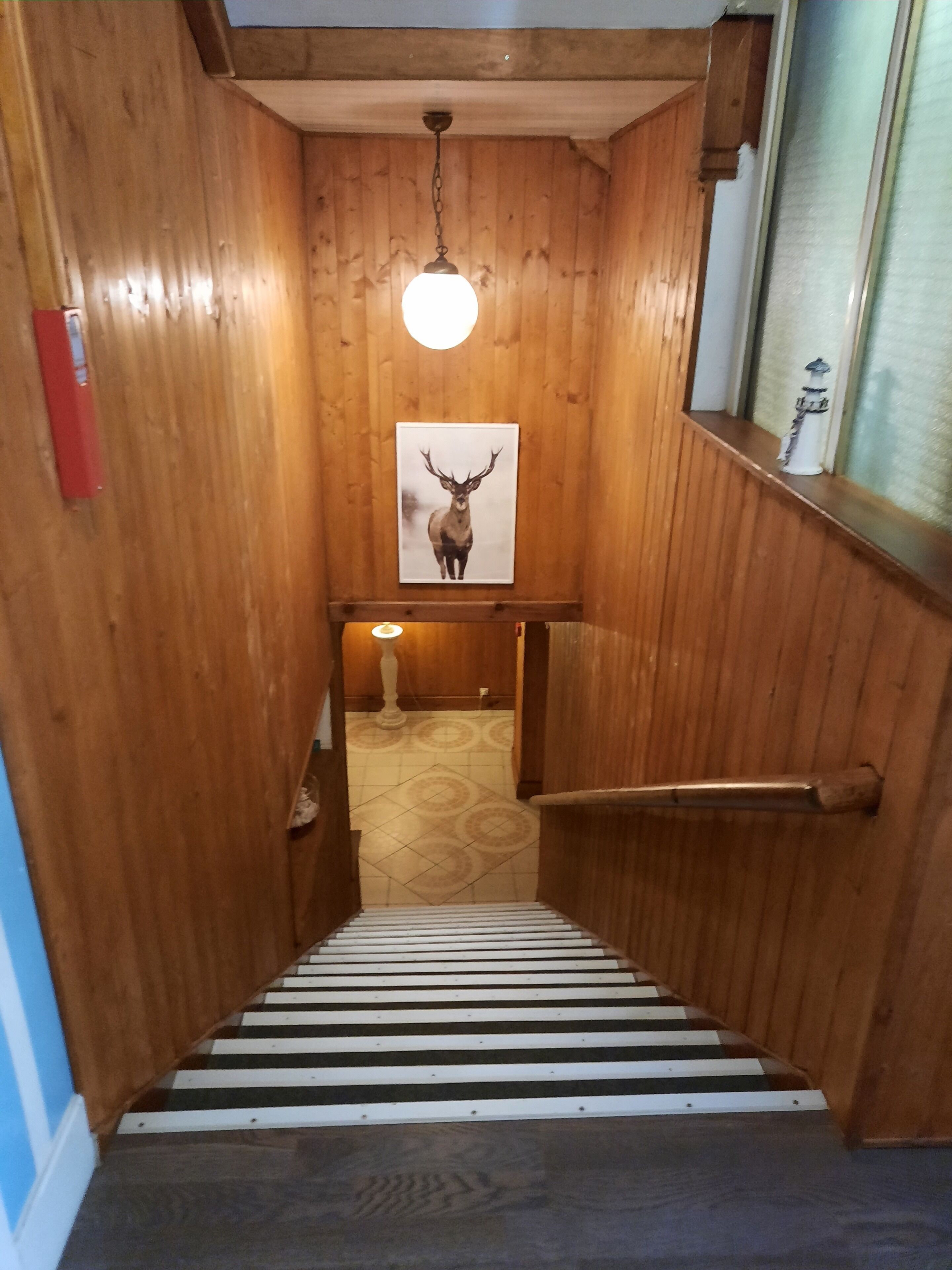 A wooden staircase with a framed deer picture, a light fixture, and a window with a water spout.