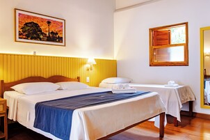 Quarto de hotel com duas camas, cabeceira de madeira, um quadro, uma janela e um espelho.
