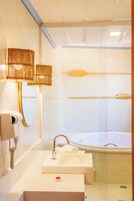 Een moderne badkamer met een witte wastafel, een spiegel, een zeepdispenser en een bad.