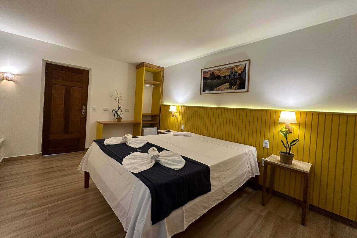 A hotel room with a bed, a desk, a mirror, and a painting on the wall.