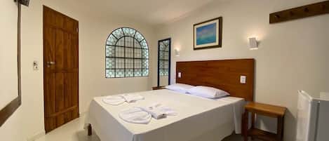 Une chambre d’hôtel avec un lit, une tête de lit en bois, une table de chevet, un téléviseur fixé au mur, une fenêtre avec vue et un tableau.