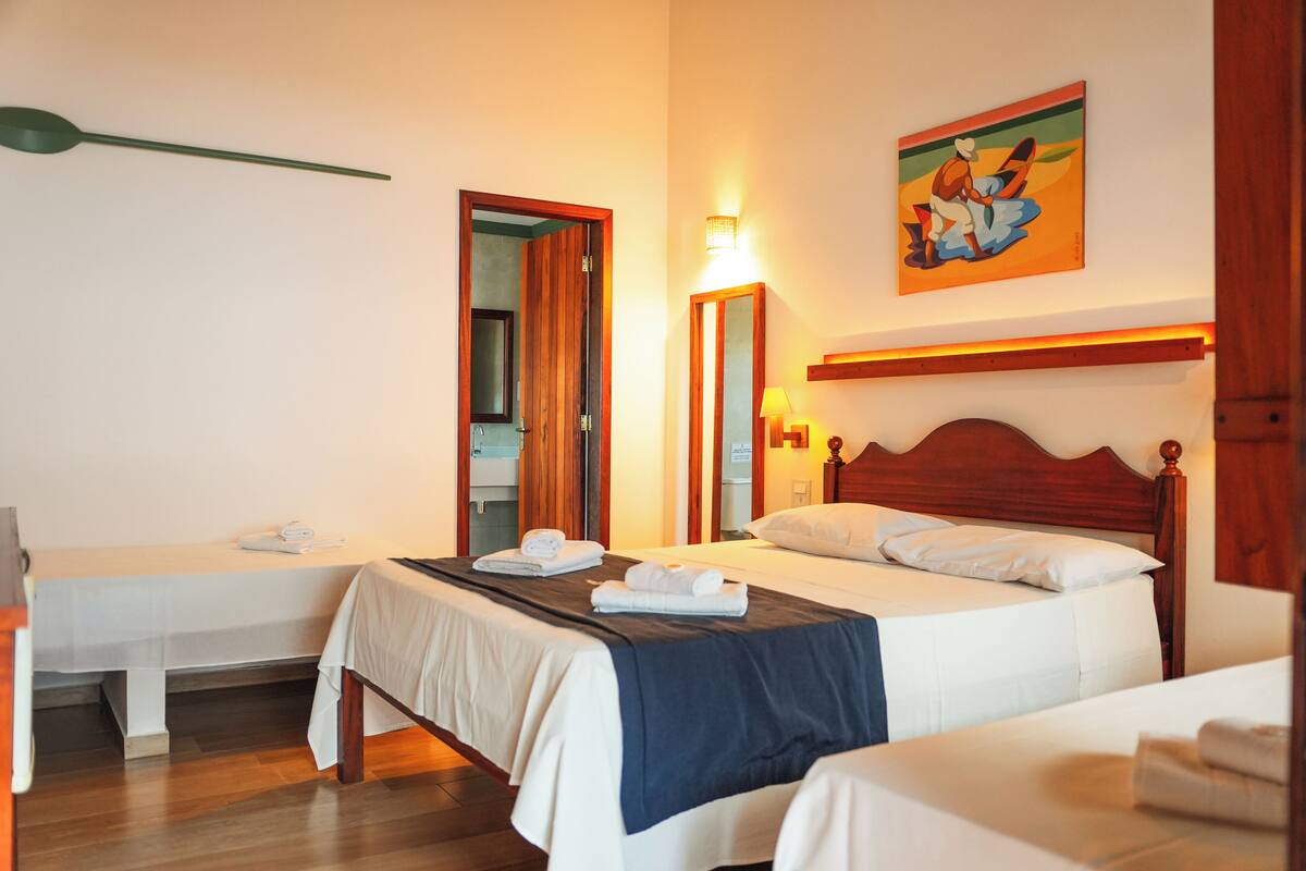 A hotel room with two single beds, a wooden headboard, a painting on the wall, and a mirror.
