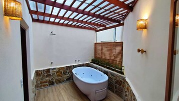 Un área de spa con pared de piedra, pérgola de madera y bañera de hidromasaje.