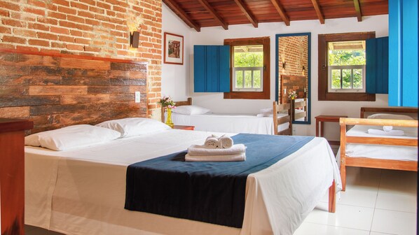 A hotel room with a brick wall, wooden ceiling, two beds, a wooden bench, and a window with blue shutters.