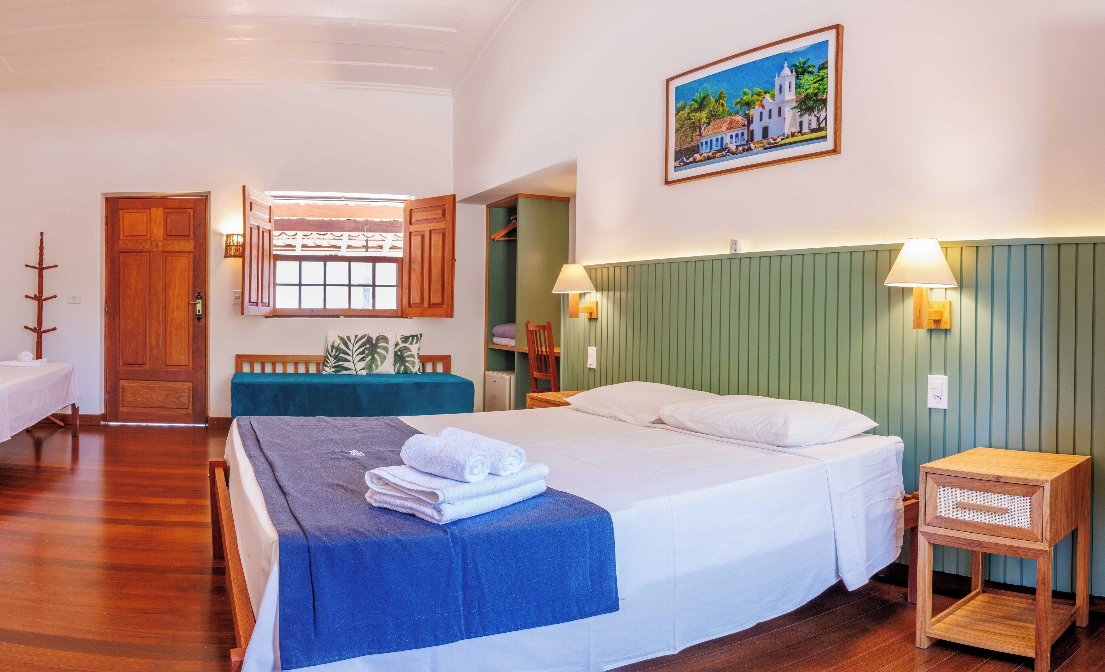 Habitación de hotel con cama, escritorio, silla, ventana con vista a un edificio y un cuadro en la pared.