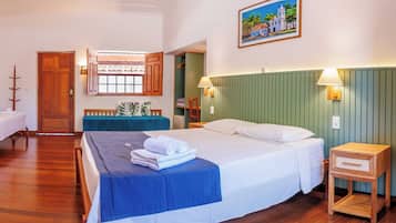 Habitación de hotel con cama, escritorio, silla, ventana con vista a un edificio y un cuadro en la pared.