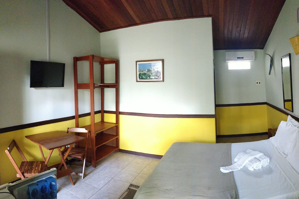 A room with a bed, a wooden chair, a small table, a TV, and a picture on the wall.