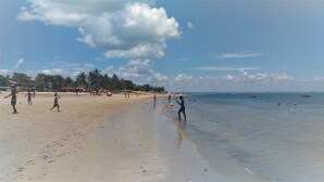 Una playa con gente jugando, un bote en el agua y palmeras al fondo.