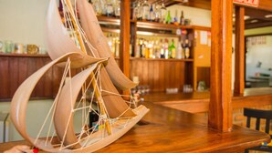 Un modelo de barco de madera sobre una barra, con una zona de bar y estantes llenos de botellas al fondo.