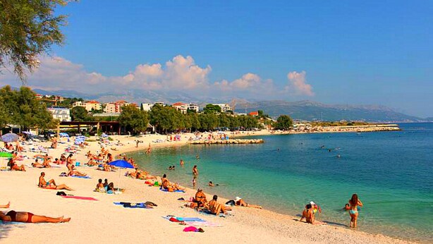 A beach with people sunbathing and swimming, a clear sky, and buildings in the background. - Apartmani Znjan (Split)