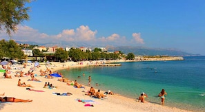 A beach with people sunbathing and swimming, a clear sky, and buildings in the background. - Apartmani Znjan (Split)
