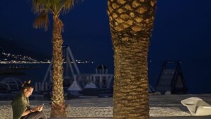 A nighttime outdoor seating area with palm trees and a view of a bridge and city lights in the background. - Apartmani Znjan (Split)