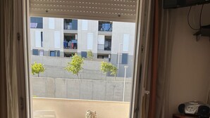 A hotel room with a bed, a small table with two chairs, and a view of a balcony with a table and chairs. - Apartmani Znjan (Split)