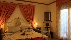 A bedroom with a four-poster bed, a nightstand with a lamp, a mirror, and a window with curtains. - Apartmani Znjan (Split)