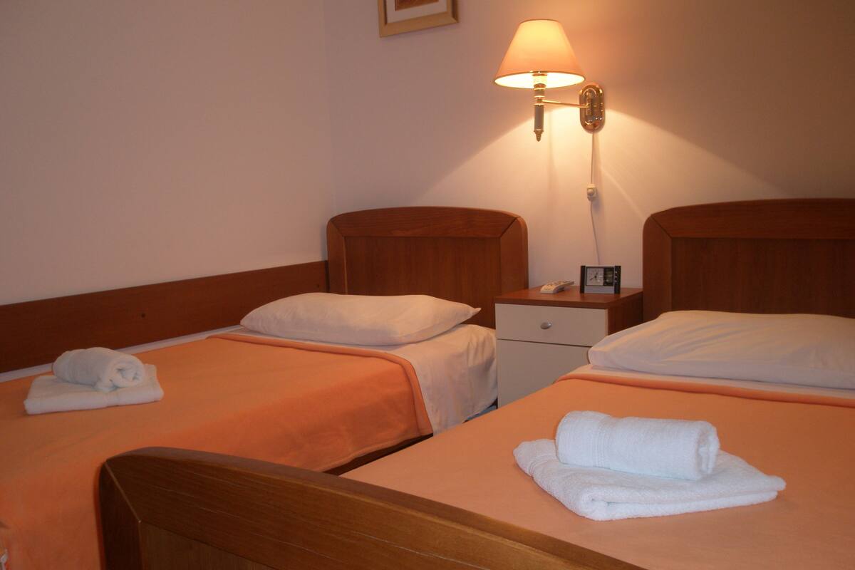 Ein Hotelzimmer mit zwei Einzelbetten, jeweils mit einem hölzernen Kopfstück, einem Nachttisch und einer Lampe.