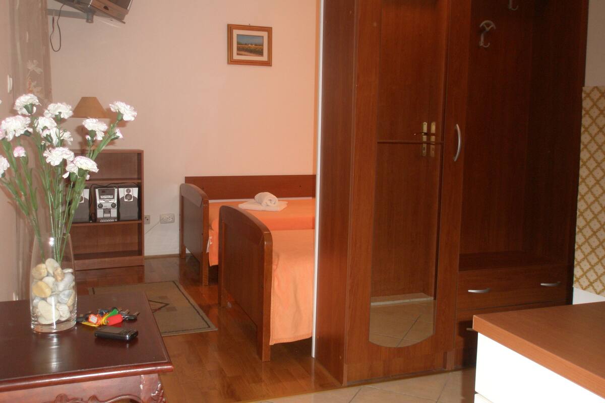 Ein Hotelzimmer mit Bett, Holzschrank, Schreibtisch mit Blumenvase und Fernseher an der Wand.