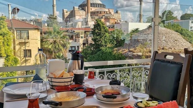 A table set for a meal with various dishes and a view of a mosque with minarets in the background. - Villa Sofia (Istanbul)