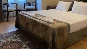A hotel room with a large bed, two chairs, a nightstand, and a patterned rug. - Villa Sofia (Istanbul)