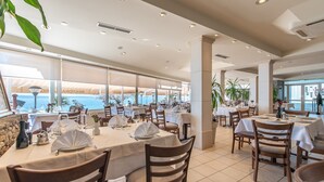 Un vaste espace dédié à la salle à manger, avec des tables disposées pour accueillir de nombreux convives, de grandes fenêtres offrant une vue sur la mer et un aménagement intérieur moderne.