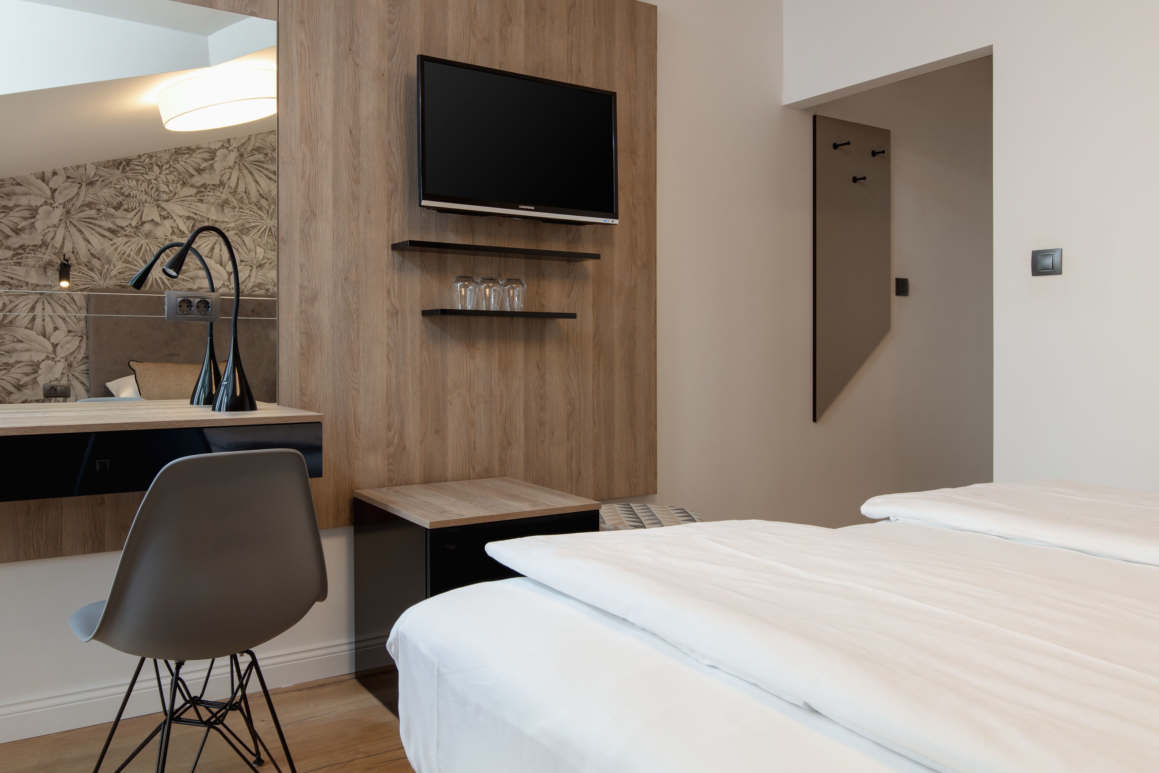 Ein Hotelzimmer mit einem Bett, einem Schreibtisch mit Stuhl, einem an der Wand befestigten Fernseher und einem Spiegel.