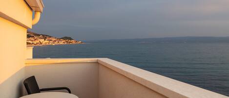 A balcony with a table and chairs, overlooking a coastal town and the sea.