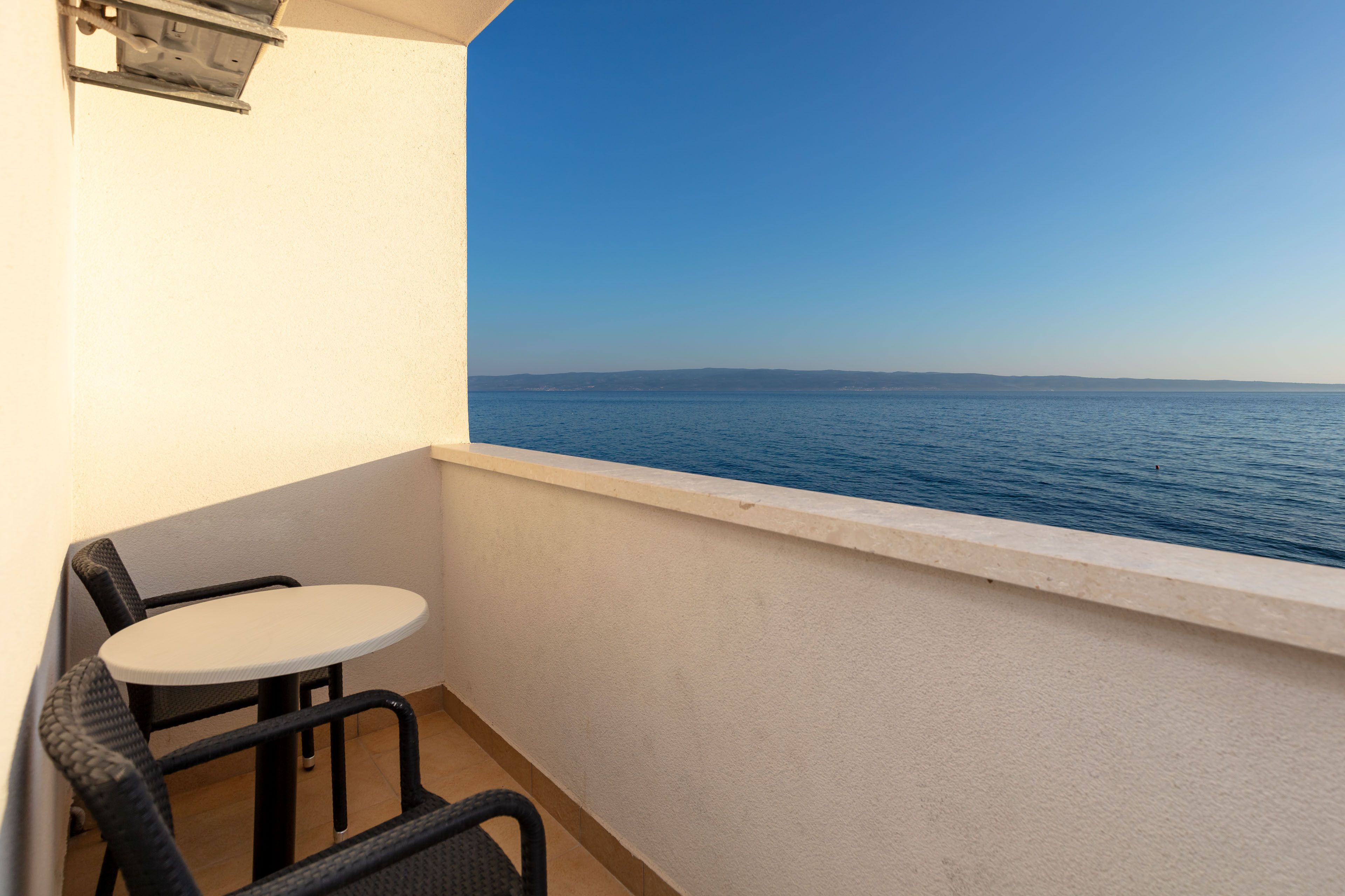 A balcony with a table and chairs, overlooking a calm sea and distant land.