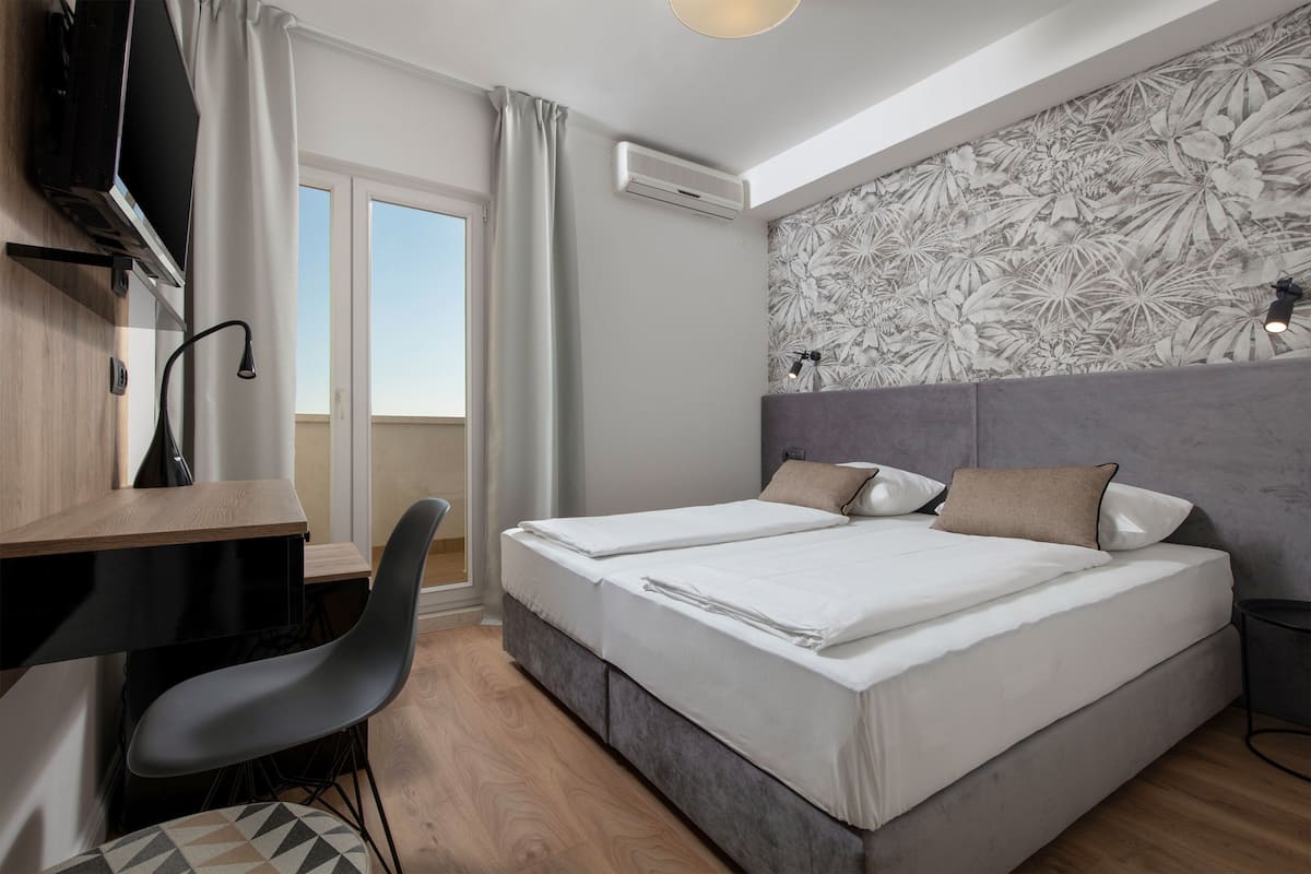 A modern hotel room with a bed, desk, chair, and a large window.