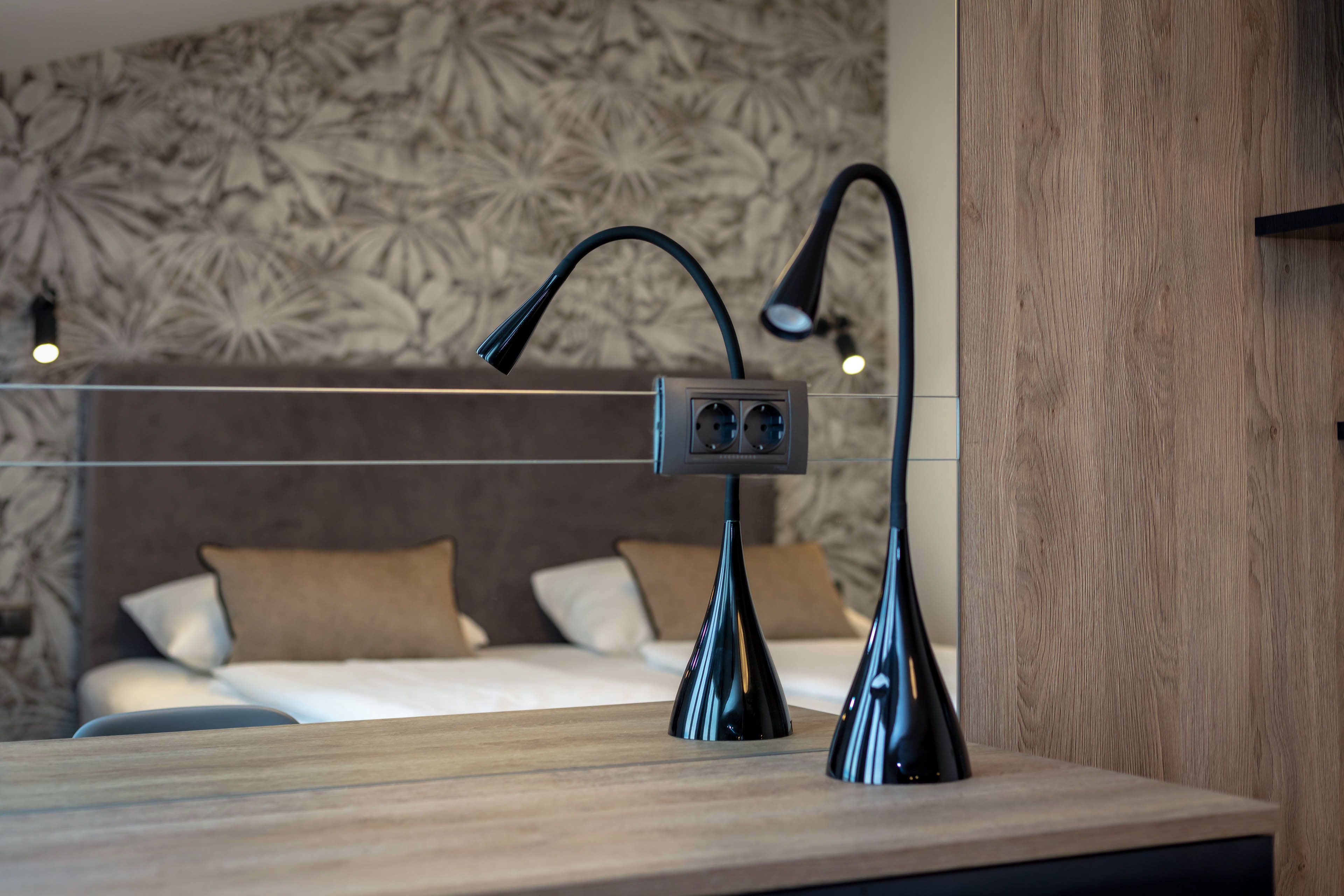 Une chambre à coucher moderne avec une tête de lit en bois, une table de chevet avec une lampe et un mur orné d’un motif de feuilles.