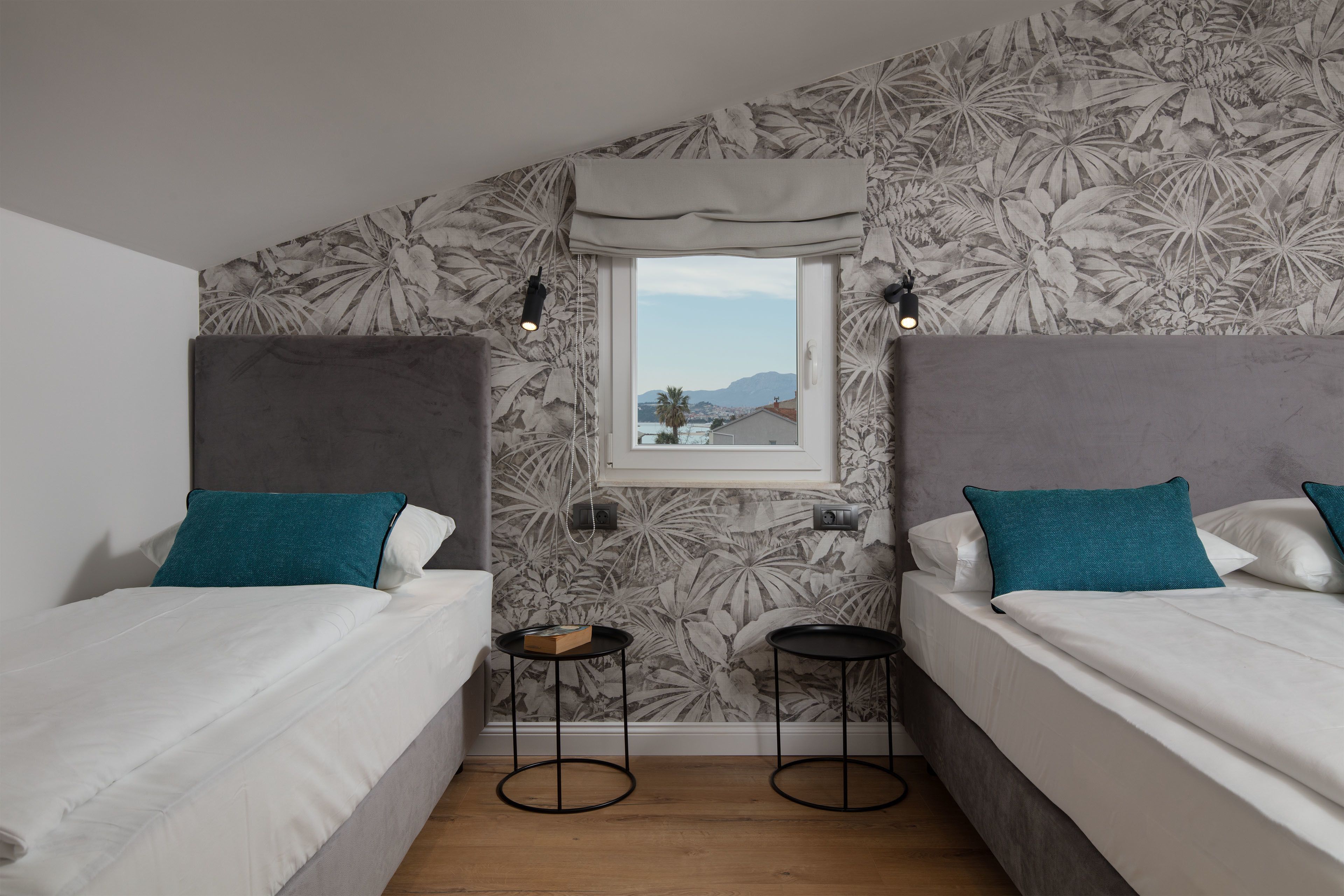 A bedroom with two single beds, a window with a view, and a floral wallpaper.