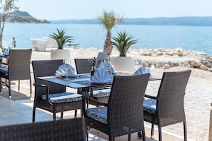 Mesa de comedor con sillas de mimbre, mantel blanco y vista al mar.
