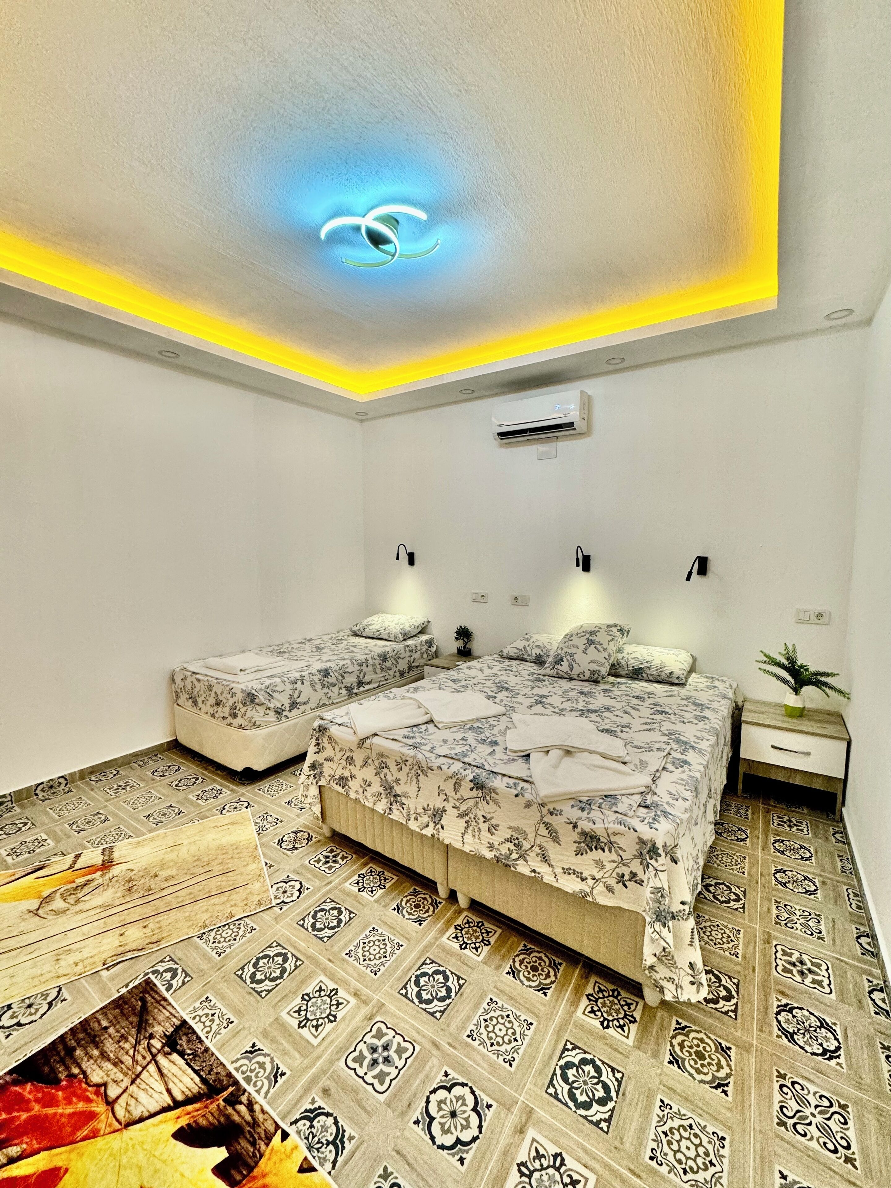 Une chambre à coucher comprenant un lit, deux tables de chevet, un climatiseur et des carreaux de sol à motifs.