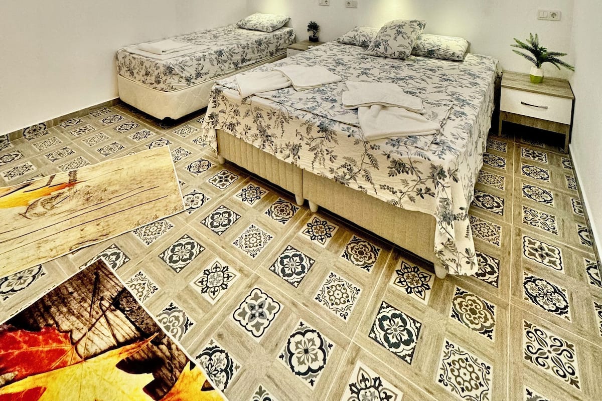 A bedroom with a bed, two bedside tables, an air conditioner, and patterned floor tiles.