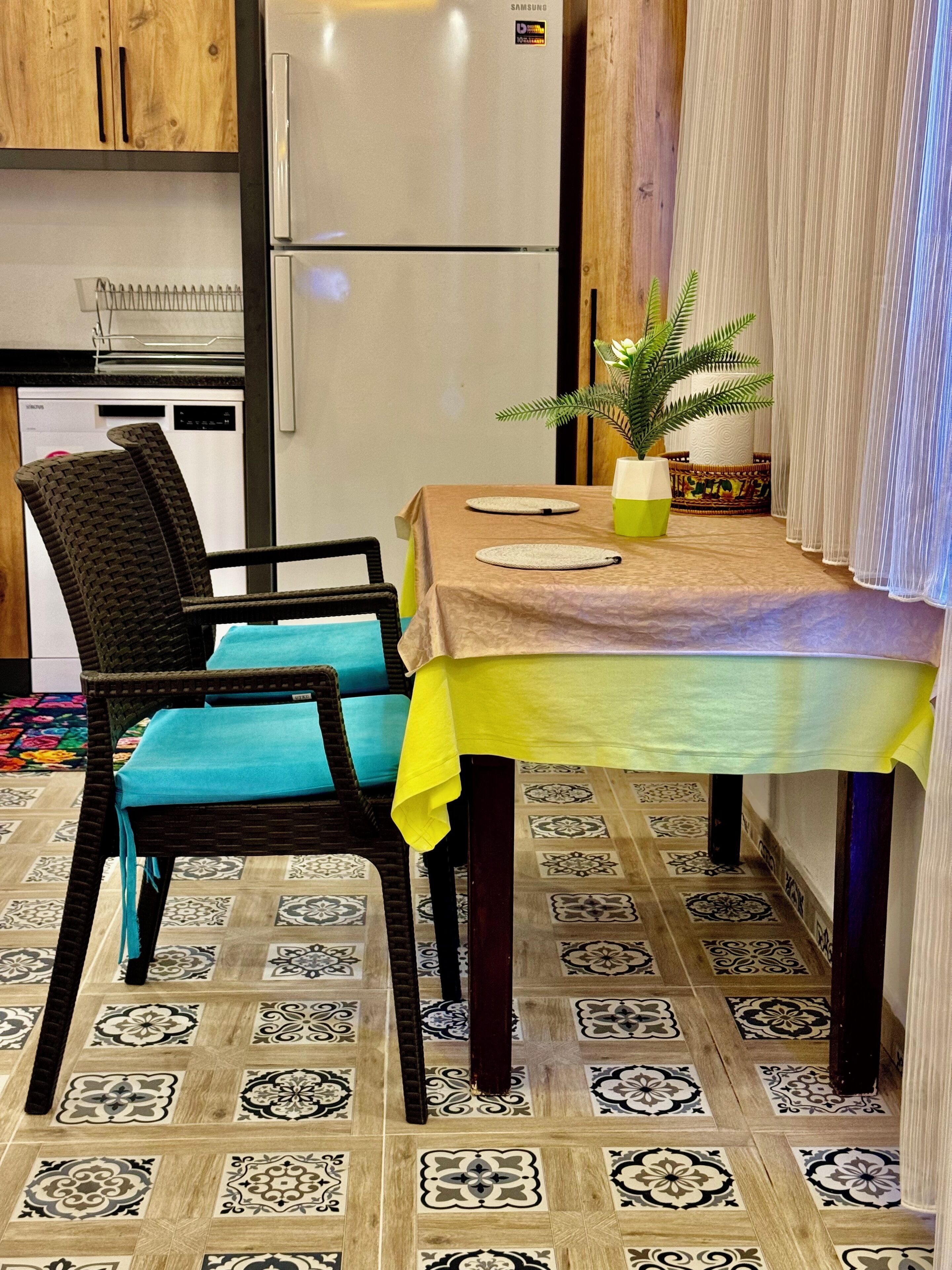 Una cocina funcional con refrigerador, una mesa de comedor con sillas y una planta en maceta.