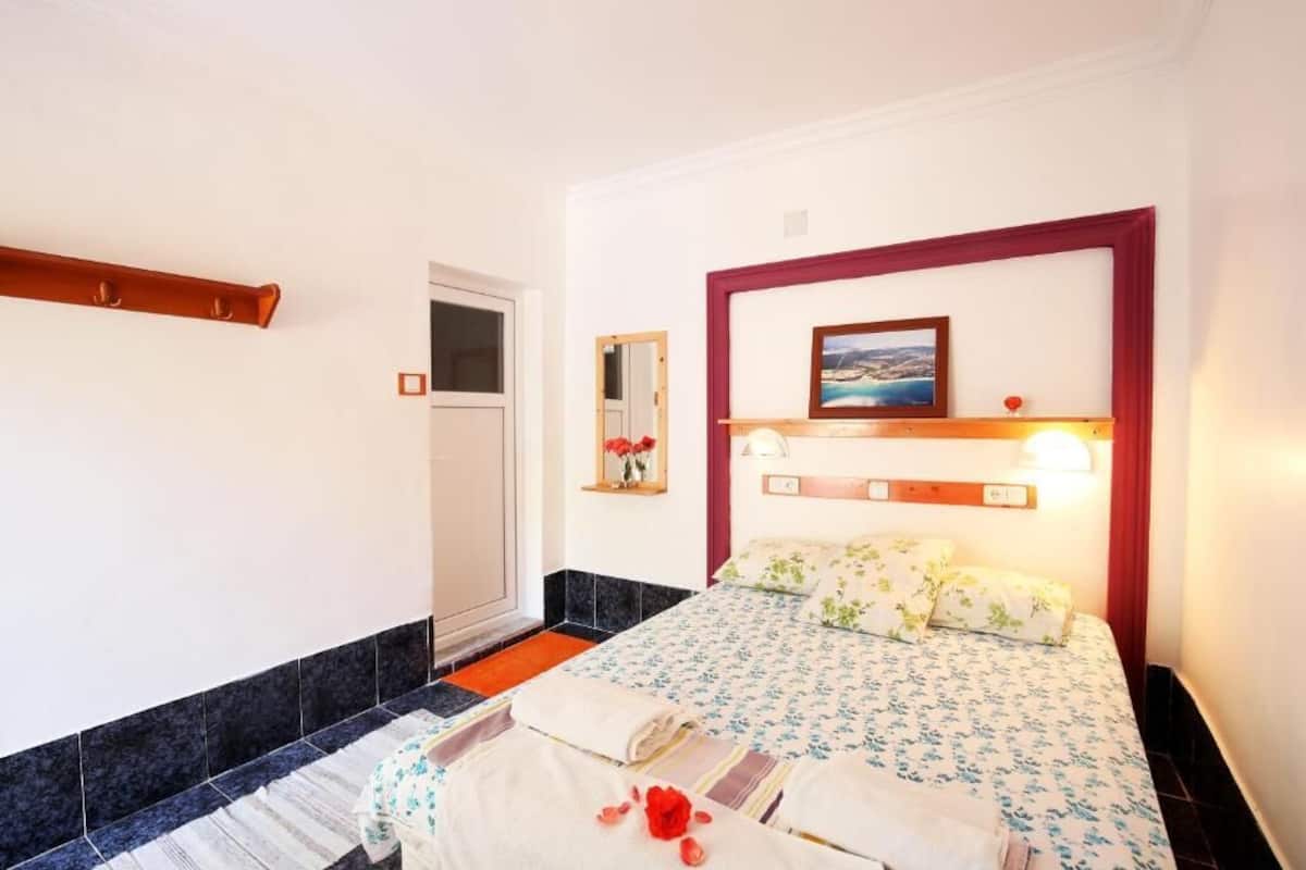 A hotel room with a bed, a nightstand, a mirror, a picture frame, and a window.