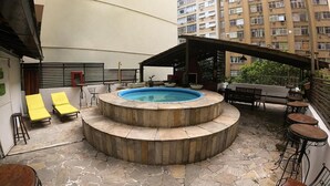 Un área de piscina en la azotea con un jacuzzi circular, sillas de descanso y mobiliario exterior.