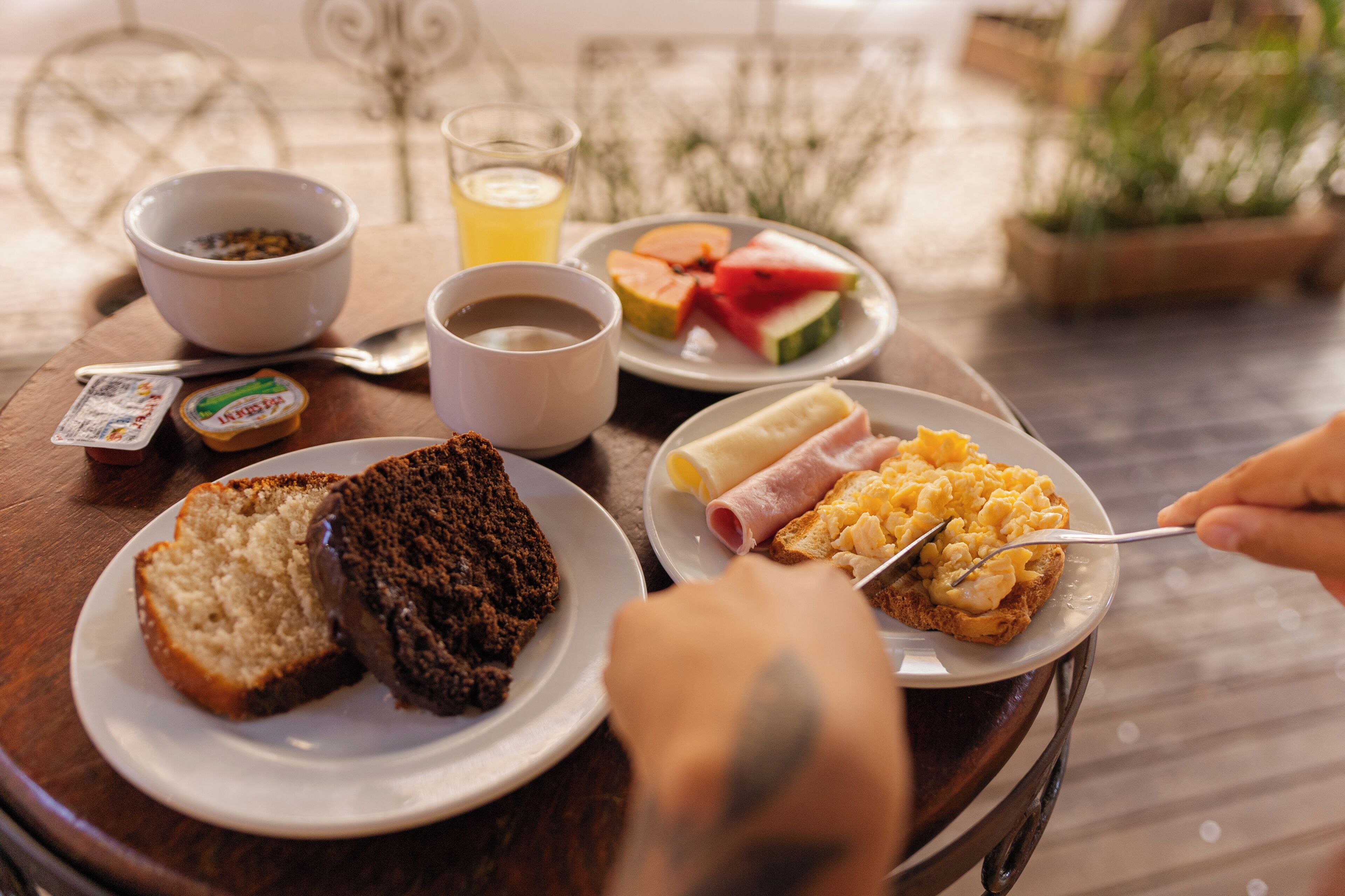 A breakfast setting with bread, eggs, and fruit on plates, a bowl of cereal, and a glass of orange juice.