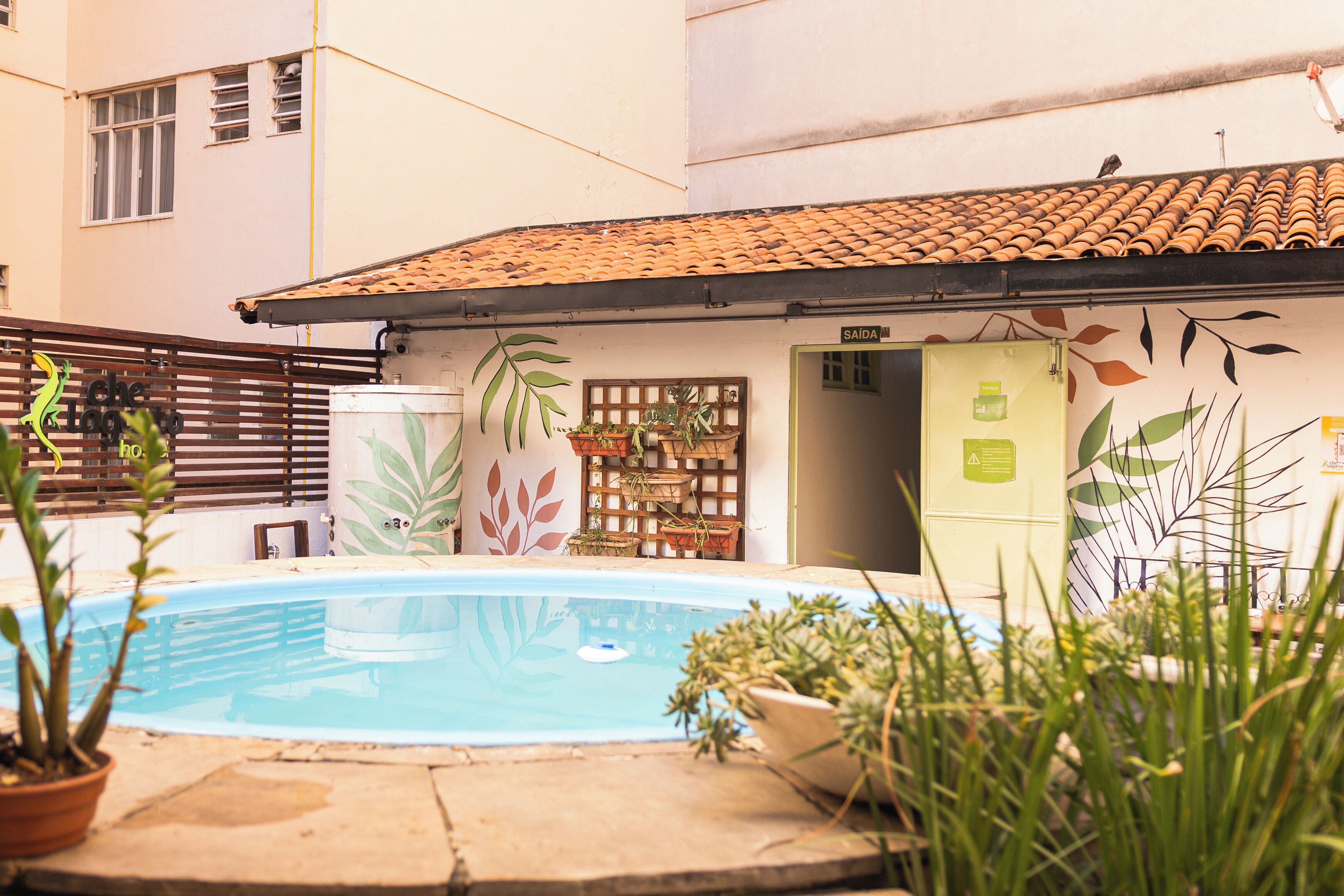 A swimming pool with potted plants, a wooden fence, and a building with a tiled roof.