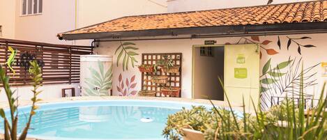A swimming pool with potted plants, a wooden fence, and a building with a tiled roof.