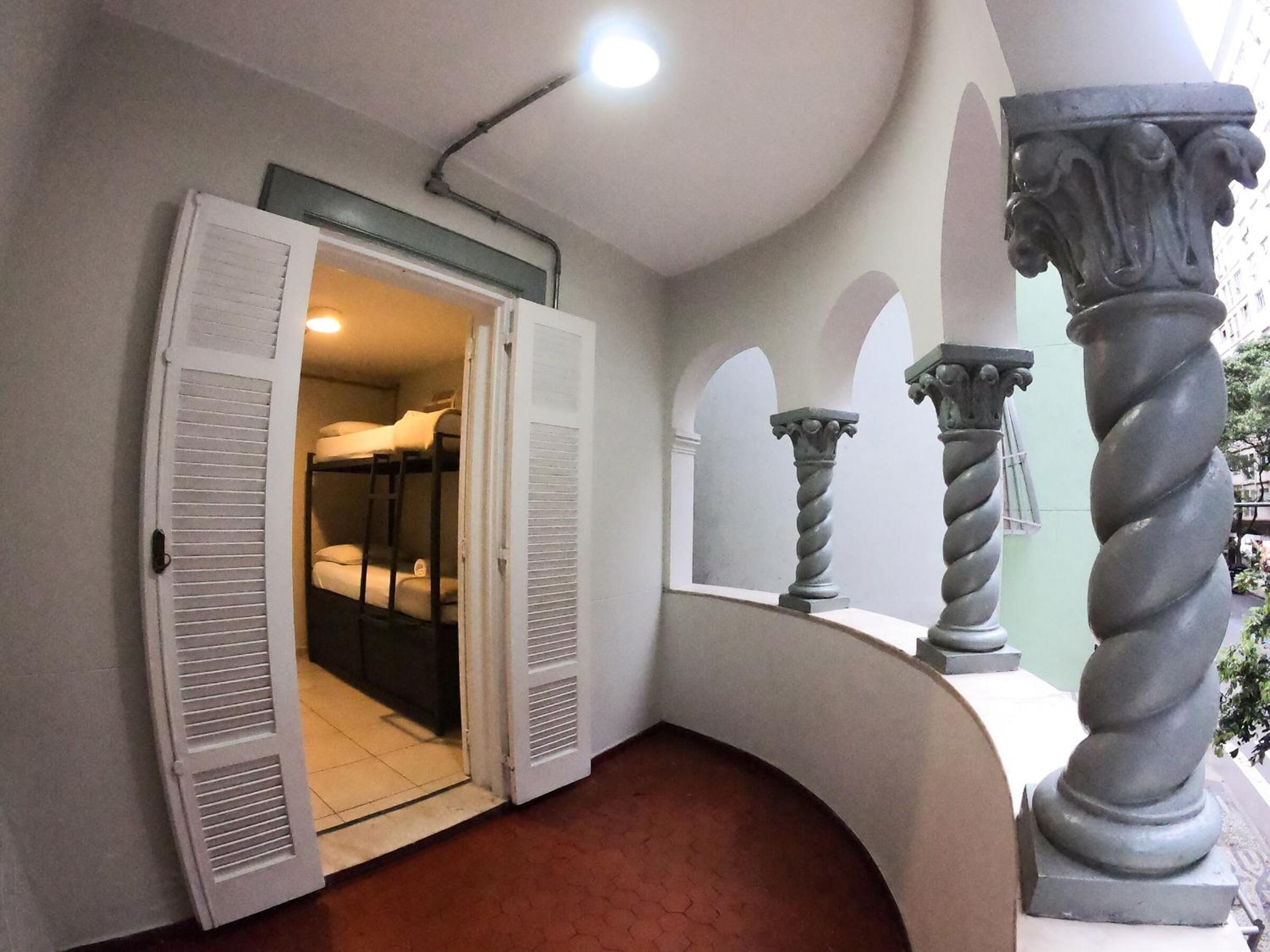 A hallway with a door leading to a room with bunk beds, a curved wall with columns, and a ceiling light.