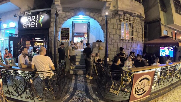 Un bar interior concurrido, con una entrada en arco de piedra, una escalera visible y suelo de baldosas.