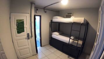 Una habitación con literas, una puerta con un letrero verde y una lámpara en el techo.