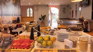 Un bufé con diversos alimentos, entre ellos frutas y postres, y un comedor con mesas y sillas.