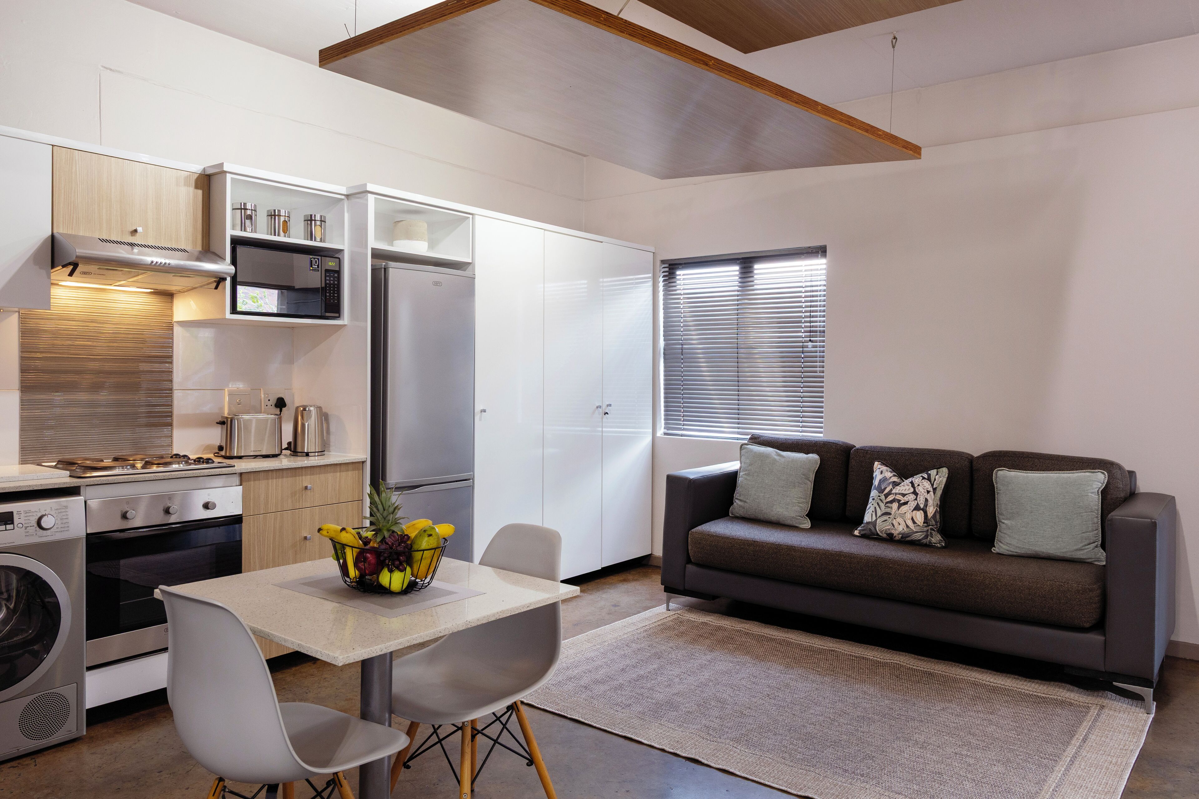 A modern kitchen with a dining area, a sofa, and a window with blinds.
