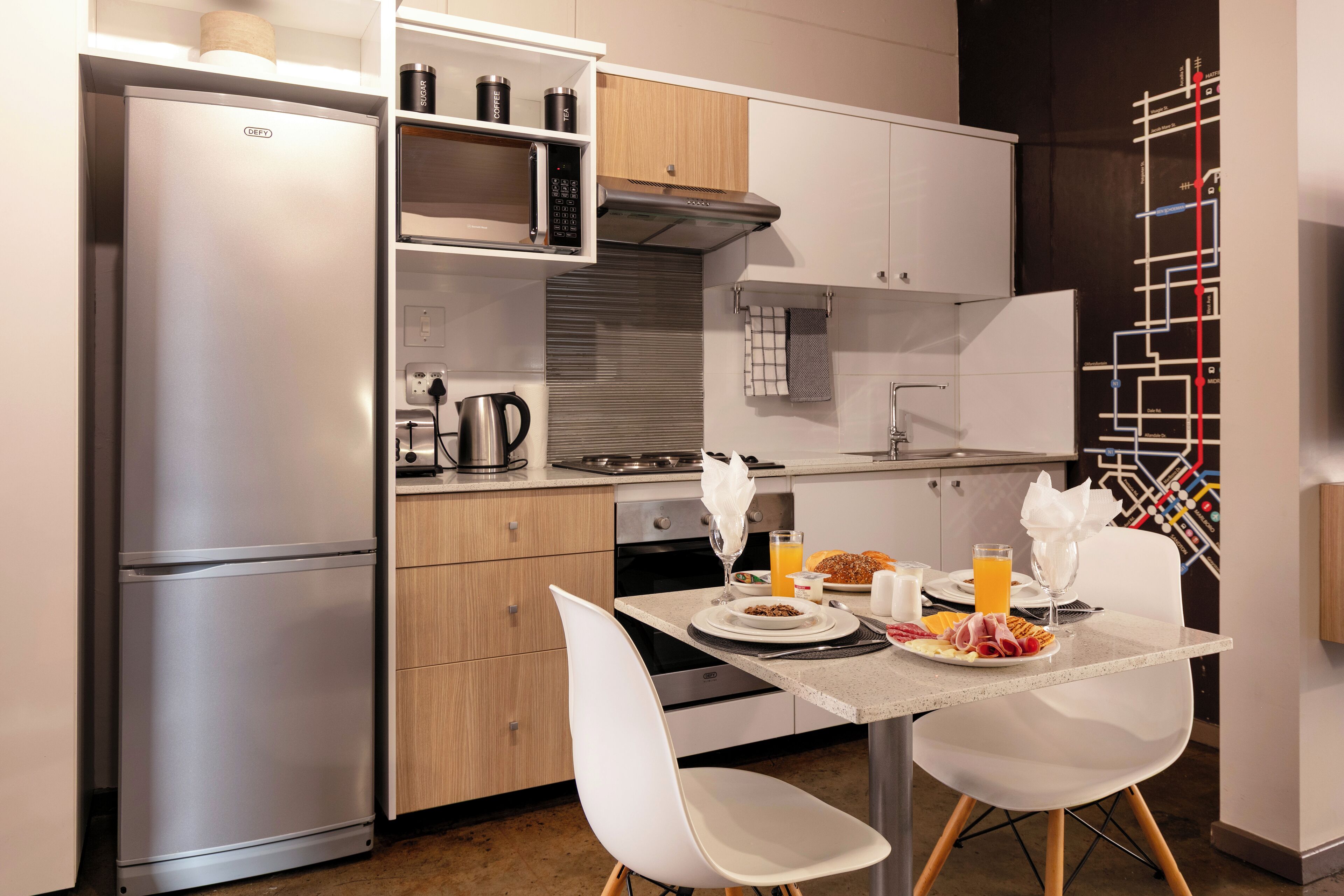 A modern kitchen with a stainless steel refrigerator, microwave, and oven. There is a dining table with chairs and a breakfast setting.