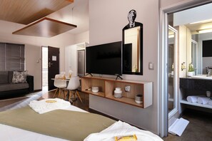 A modern hotel room with a large bed, a TV, a desk, and a bathroom with a mirror and sink.