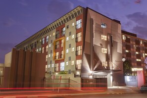Een meerlaags hotel met een modern architectonisch ontwerp, met een opvallende ingang met een luifel en een herkenbaar bord met de tekst 
